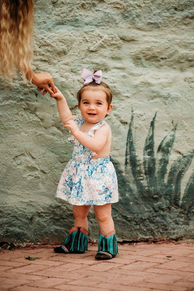 Child in a floral cowgirl dress standing on a brick path with a textured wall background