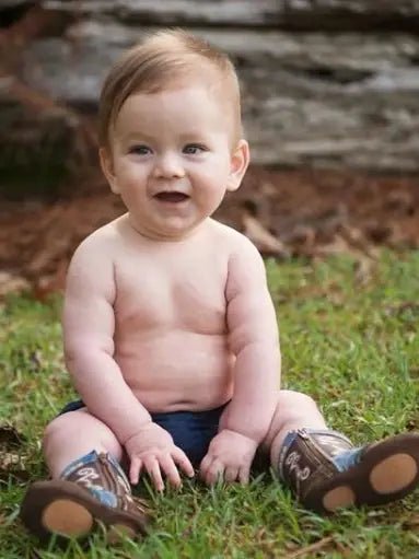 Infant in Nash boots sitting on grass in romper