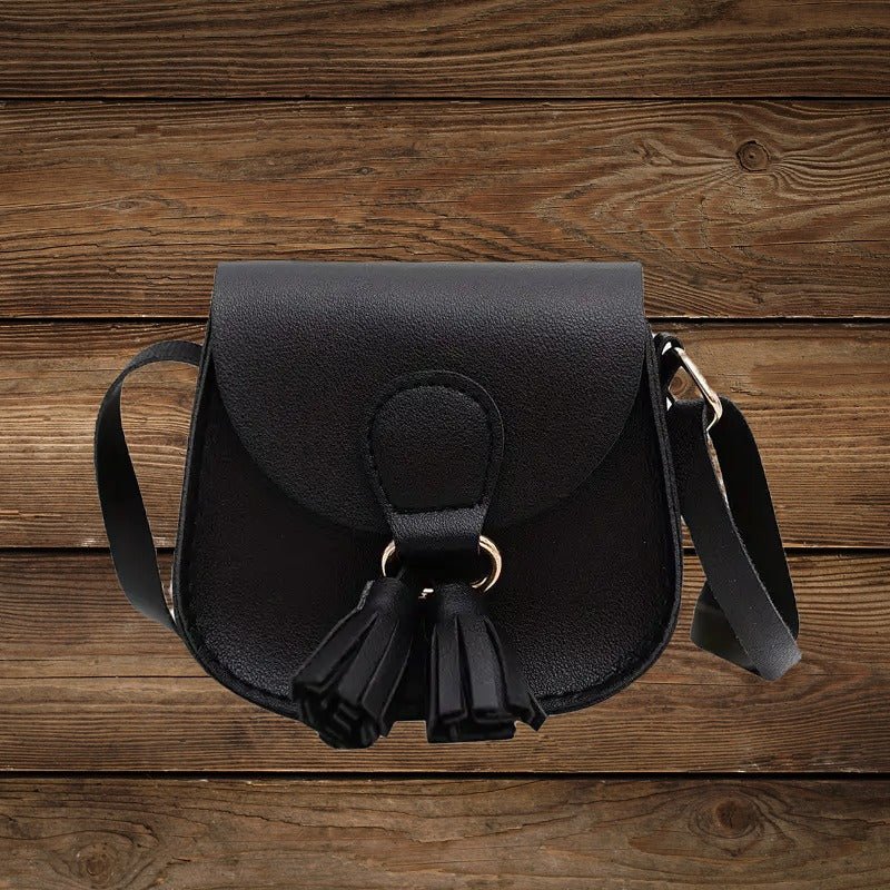 Black mini crossbody purse with tassel detail on wood background.