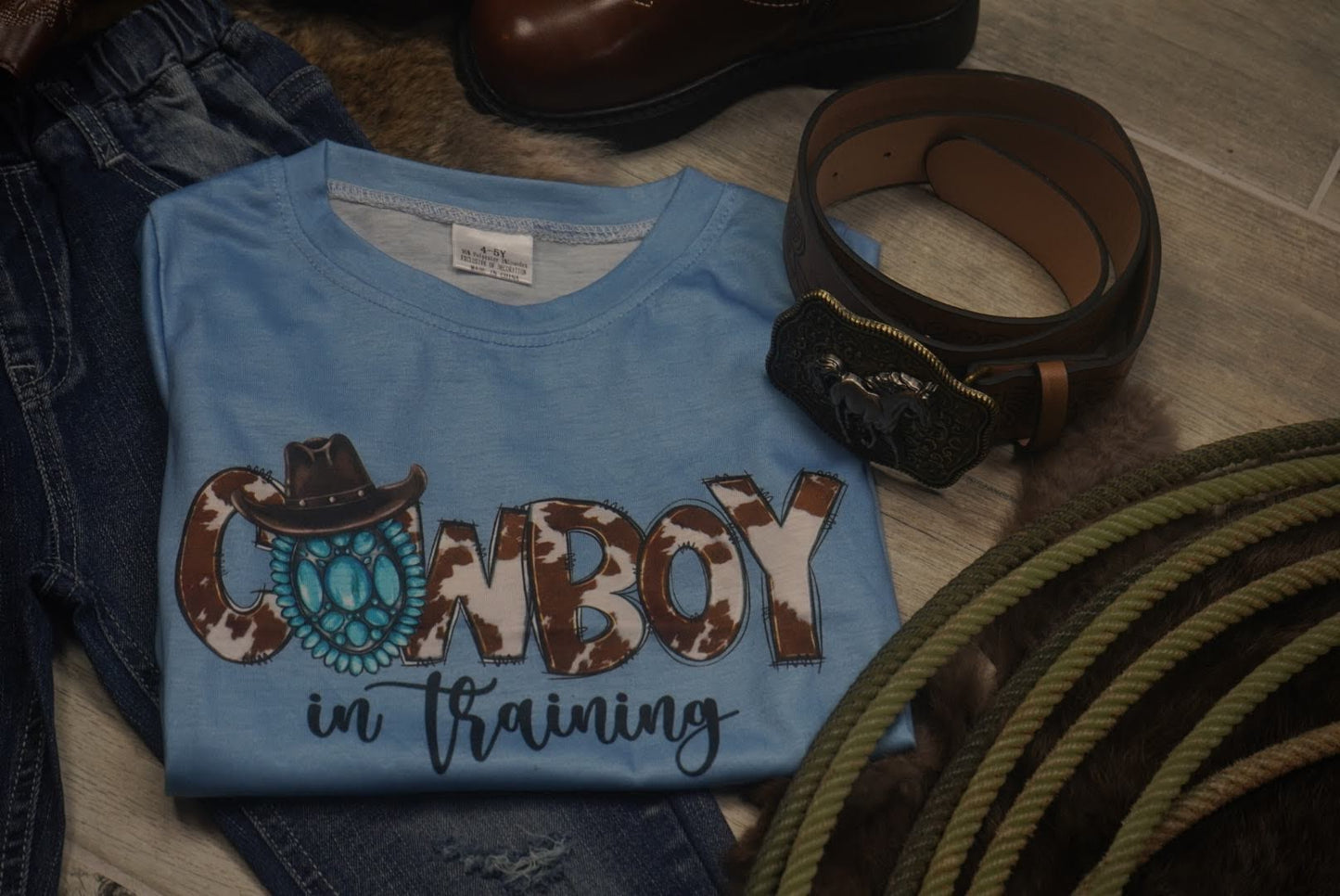 Folded blue cowboy kids shirt styled with jeans, belt, and rope for western look