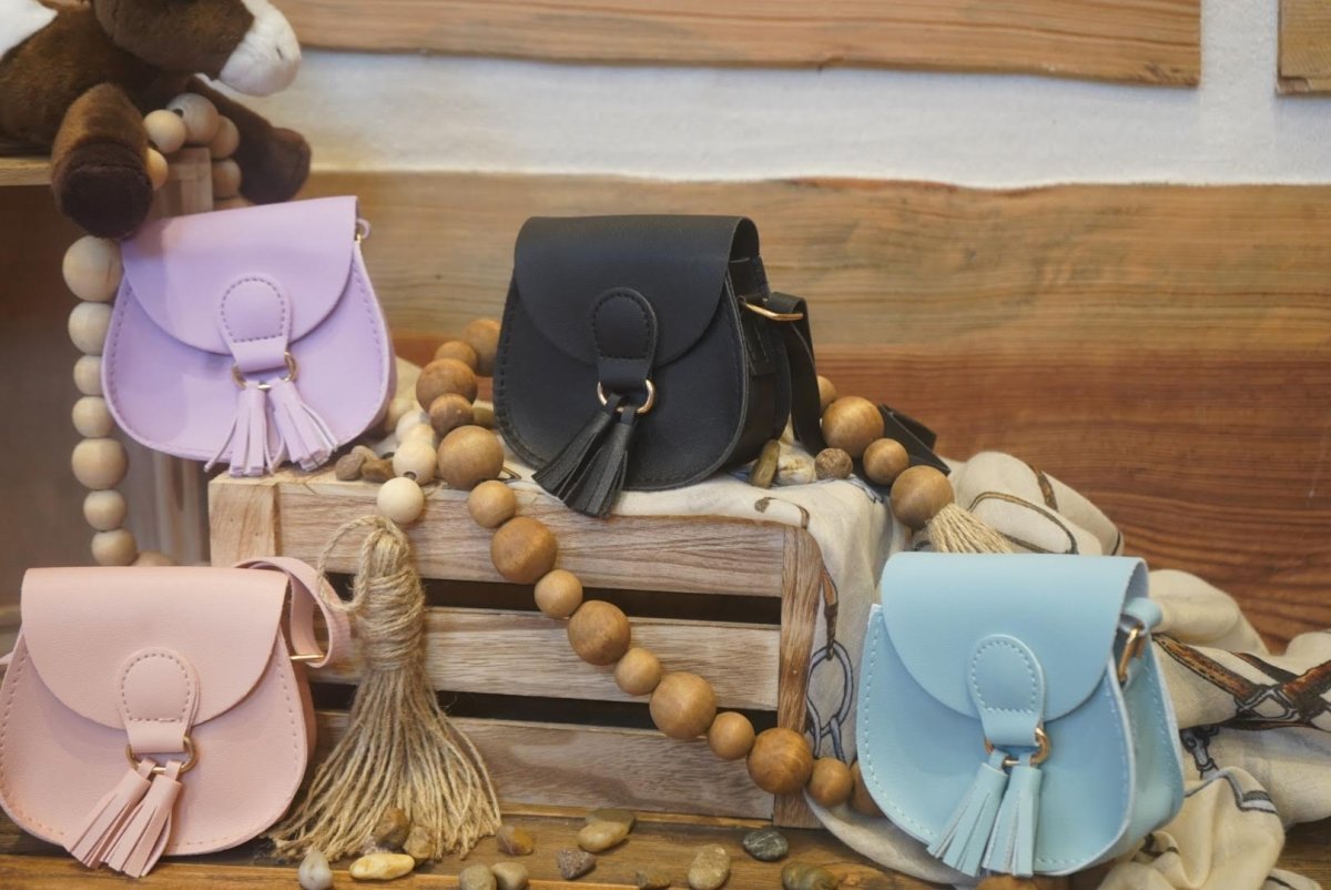Colorful mini crossbody purses for kids with tassels, displayed on rustic wooden crates.