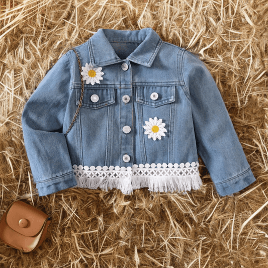 Toddler western denim jacket with daisy patches and fringe hem displayed on straw background.
