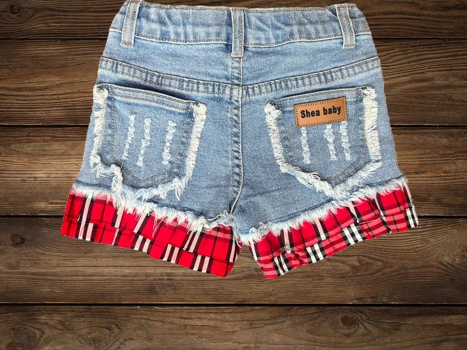 Flat lay of toddler cowgirl denim shorts with red plaid ruffle trim