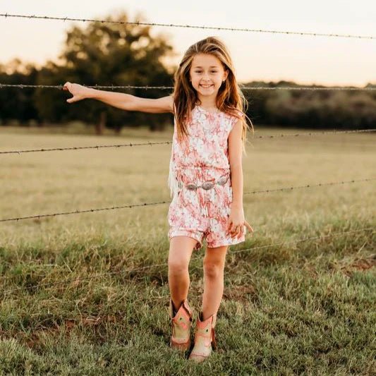Cowgirl wearing girls pink plaid fringe romper posing confidently in pasture.
