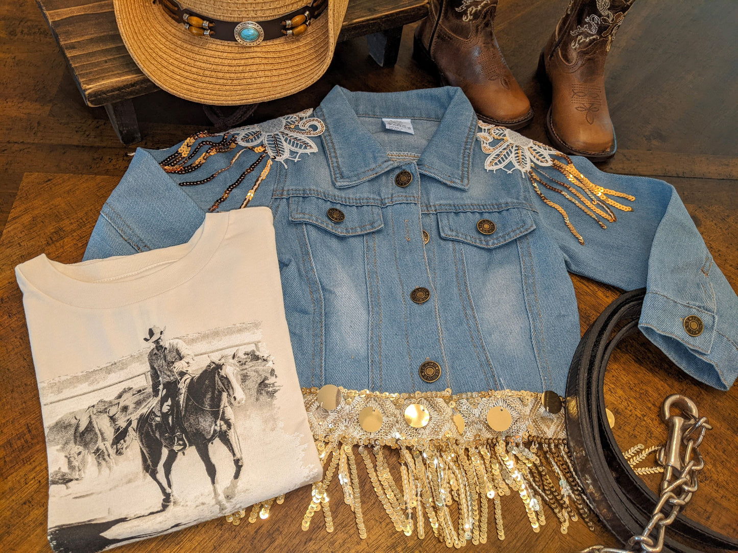 Western-themed flat lay featuring Glitter & Glamour Girls' Sequin Tassel Denim Jacket with fringe, hat, boots, and tee.