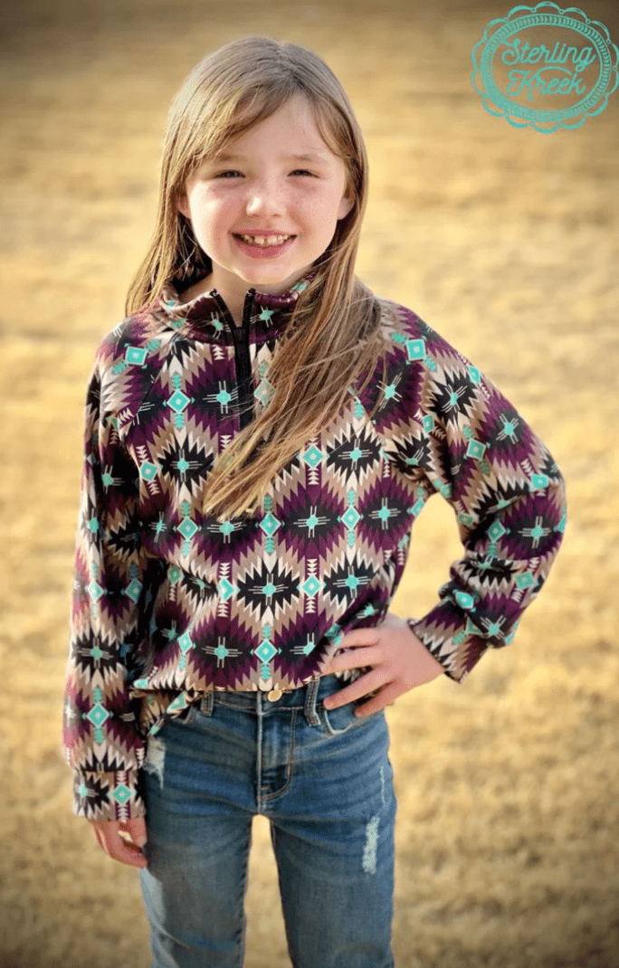Smiling girl in Mini Badlands Pullover with dark purple and turquoise Aztec design, cozy and stylish for western adventures.