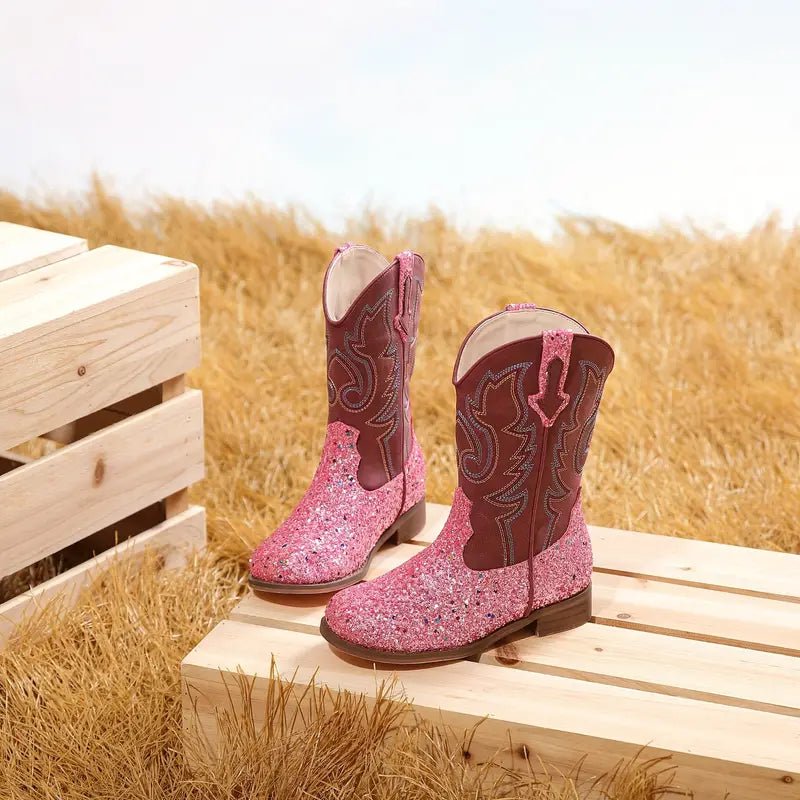 Pink glitter cowgirl boots on straw and wood background
