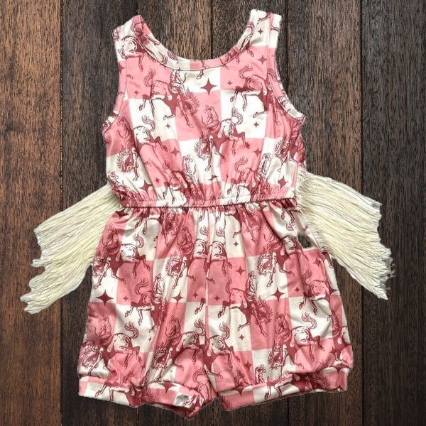 Flat lay of pink plaid bucking horse romper with fringe on wooden background.