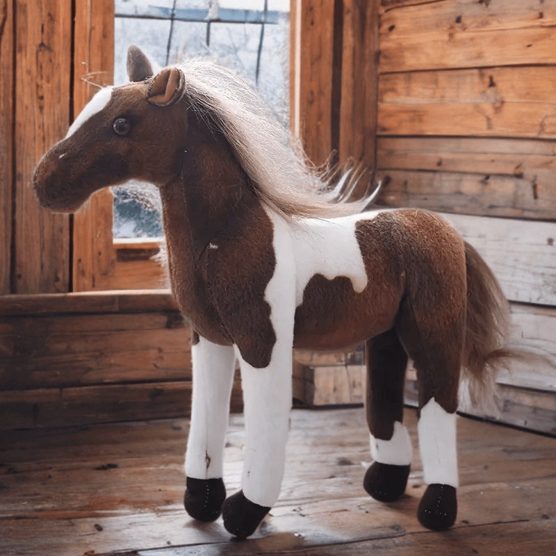 Realistic dark brown and white horse plush toy standing in wooden barn