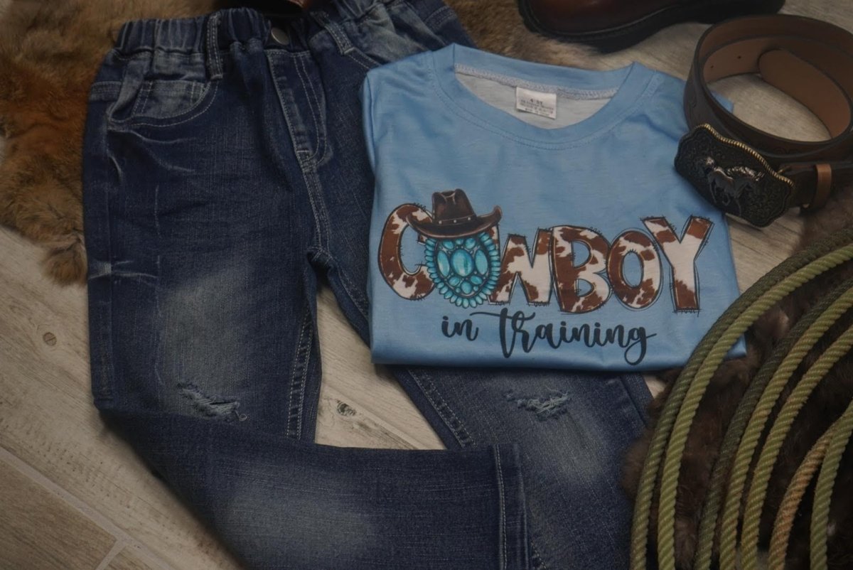 Western outfit flat lay with boys' denim ripped jeans and cowboy-themed shirt.