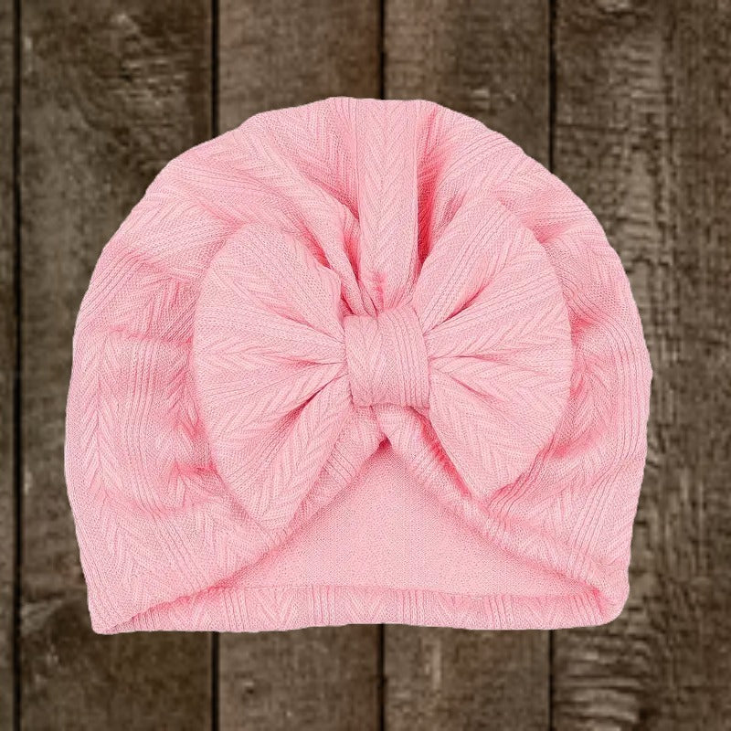 Soft pink baby cowgirl bow turban hat with large bow on rustic wooden background.