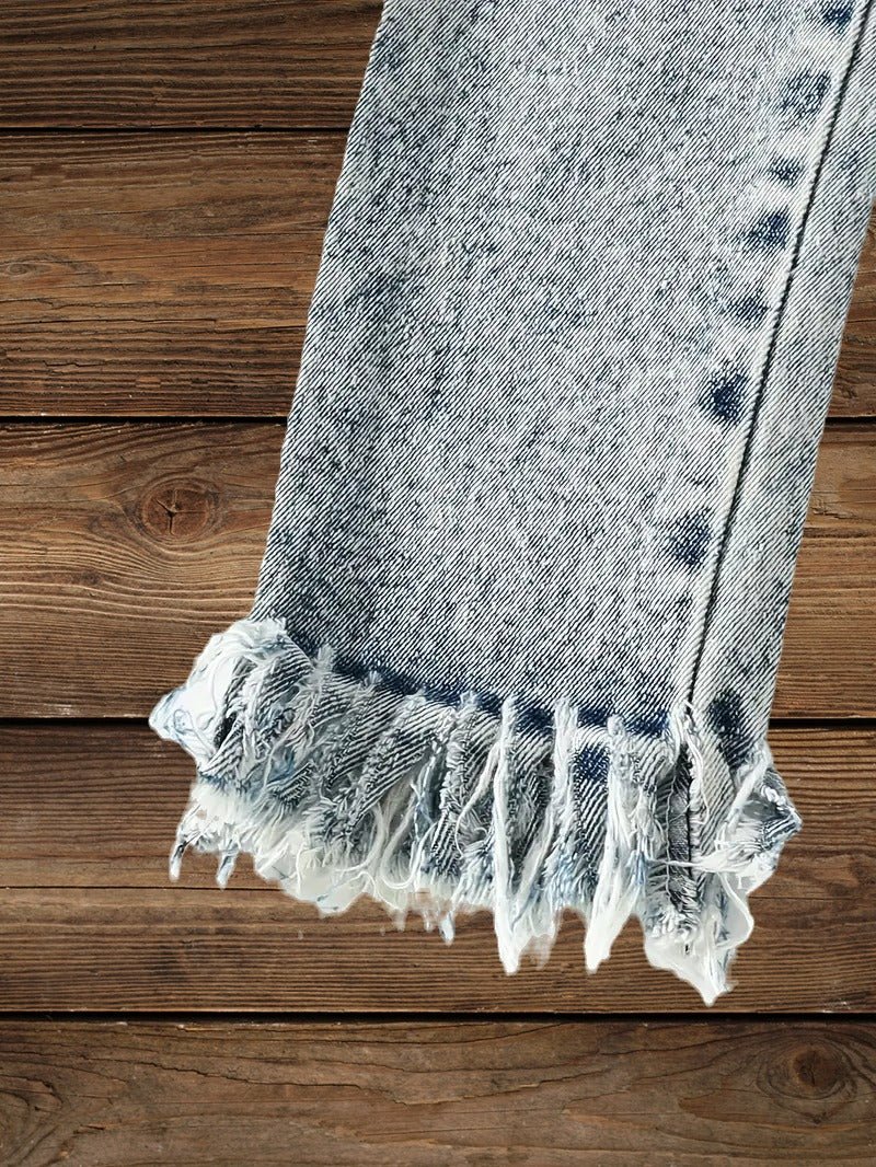 Close-up of tassel hem detail on light wash jeans