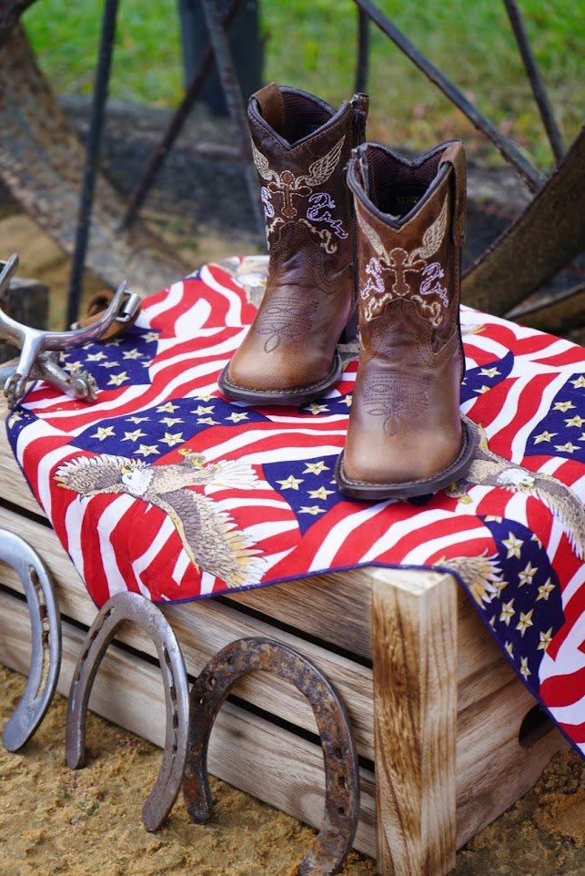 Pair of Tuffrider kids' Western boots displayed on patriotic cloth with horseshoes.