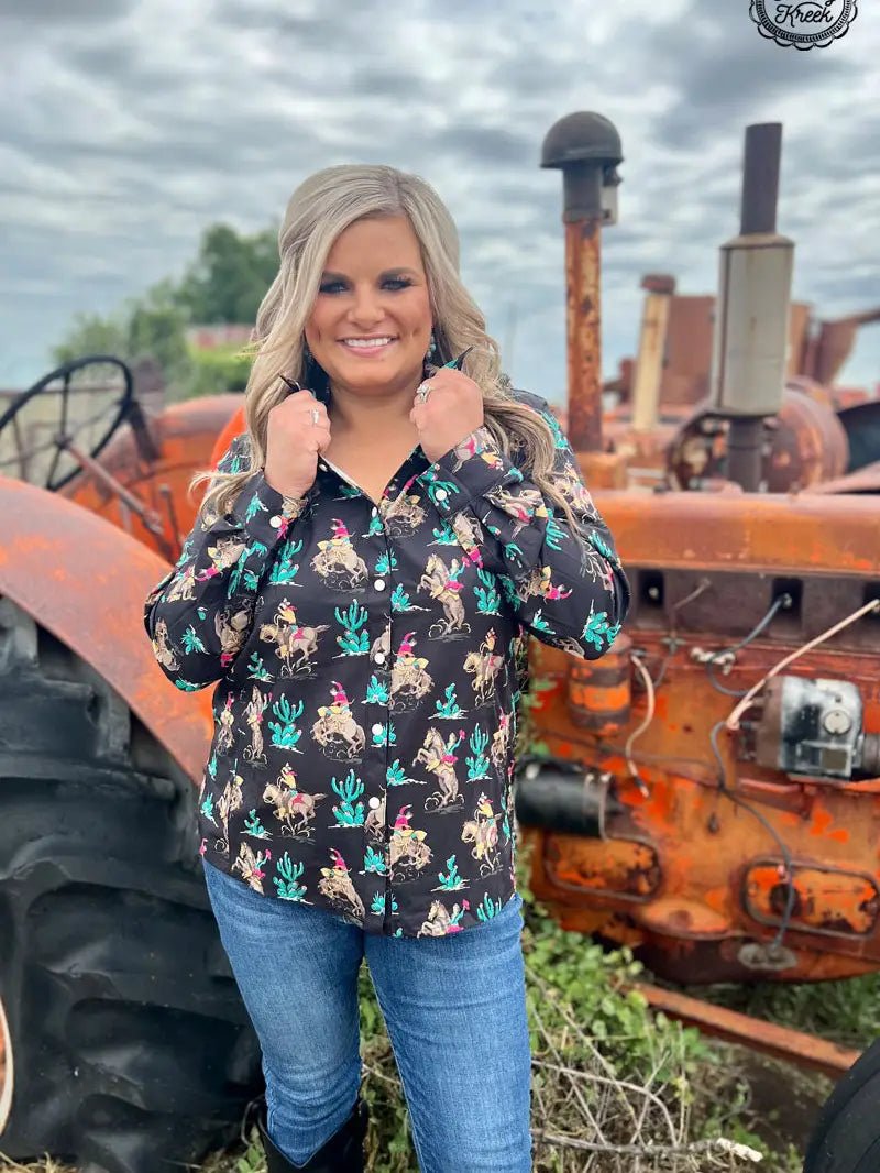 Woman in black rodeo print western shirt, standing in front of rustic tractor.
