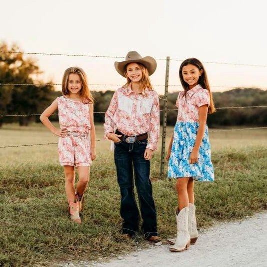 Group of girls wearing Western Kids Emporium outfits including pink plaid romper, shirt, and blue dress.