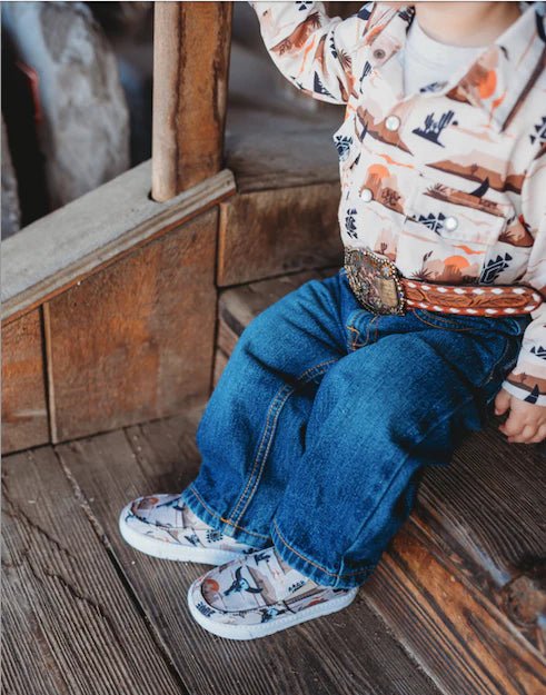 Child wearing cowboy-themed sneakers beside rustic wood porch