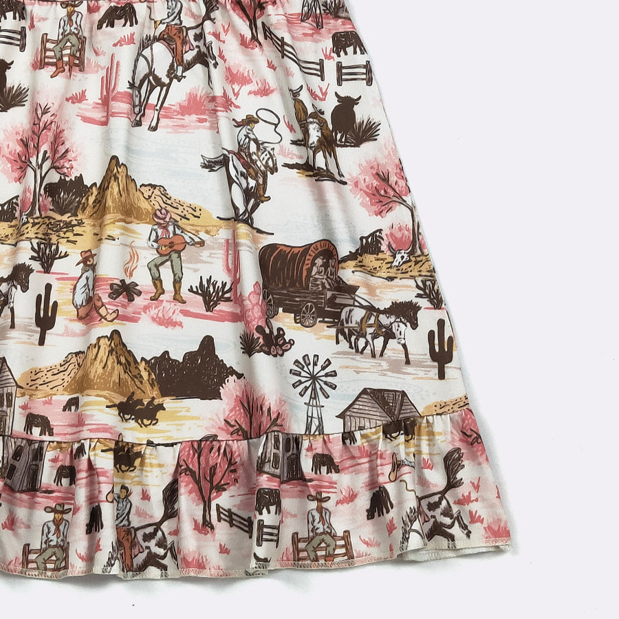 A close-up of a tiered skirt featuring a detailed western landscape print with cowboys, covered wagons, cacti, and mountains in brown, pink, and beige tones on a white background.