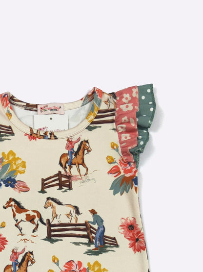 A close-up of a children's short-sleeve top with a cream base, featuring a western equestrian print of horses, fences, and riders. The sleeves have ruffled trim in green and pink patterns, set against a plain light gray background.