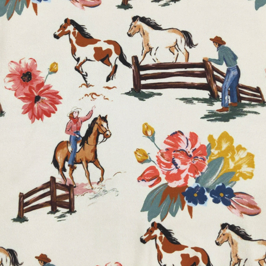 A close-up of a fabric or wallpaper pattern featuring a western theme with horses, cowboys, fences, and large flowers on an off-white background.