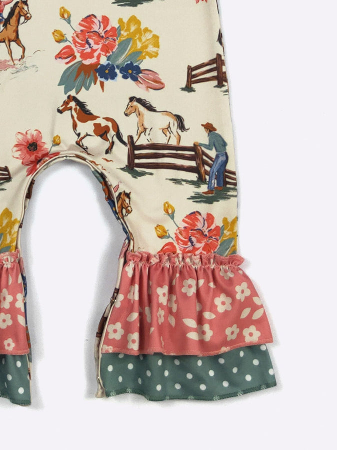 A close-up of a children's garment featuring a western-themed print with horses, fences, and flowers on a cream background, with ruffled trim in pink floral and green polka dot fabric.