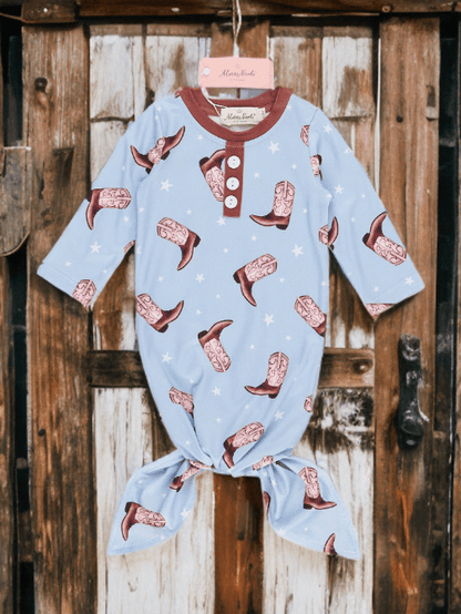 Baby onesie with cowboy boot pattern hanging on a wooden door