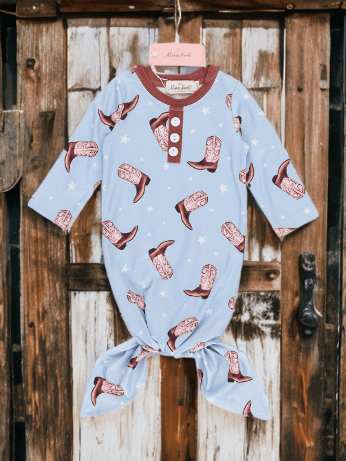 Baby onesie with cowboy boot pattern hanging on a wooden door