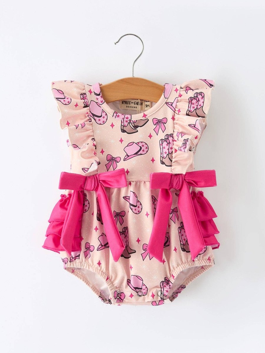 Baby romper with pink bows and cowboy print on a hanger against a white background