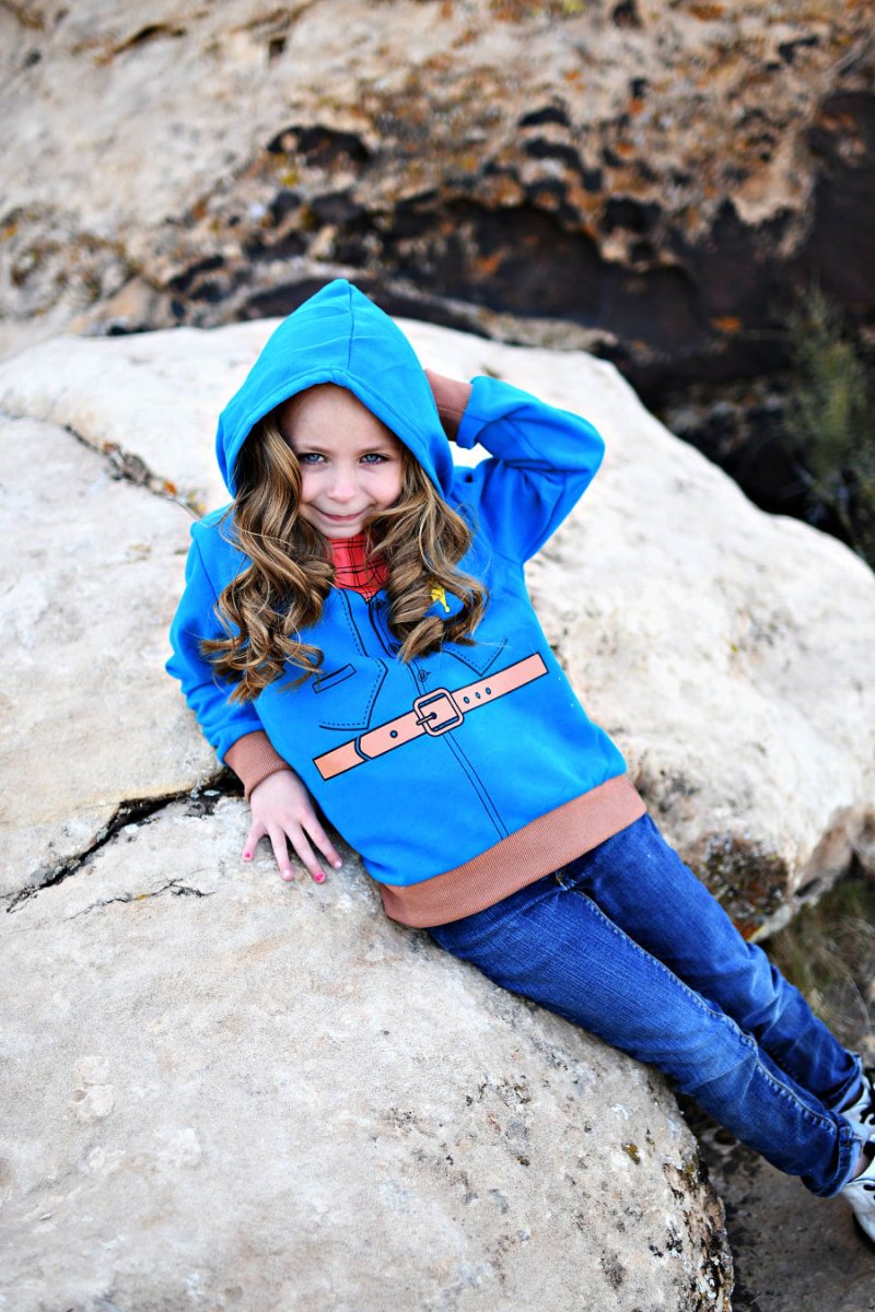 Child wearing a blue hooded jacket with a belt, sitting on rocks.