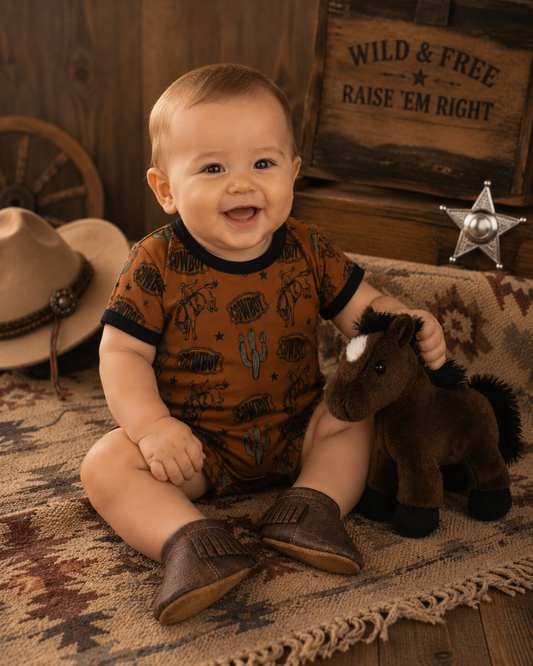 Baby in a cowboy-themed outfit with a plush horse, surrounded by rustic decor.