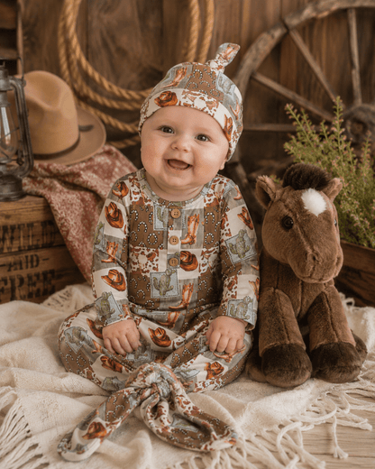 Baby in a rustic setting with a horse plush toy, cowboy hat, and lantern.