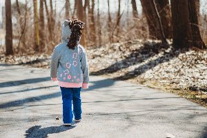Child walking away on a path in a forested area in a horse hoodie