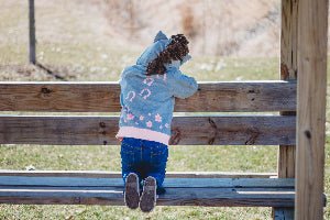 Child in a gray jacket sitting on a wooden bench outdoors