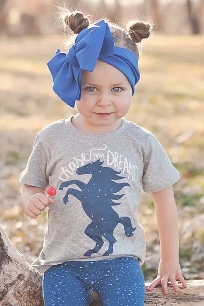 Child wearing a gray t-shirt with a horse graphic and blue headband outdoors.