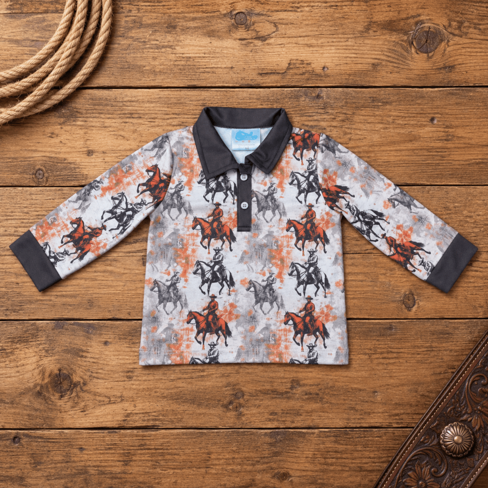 A long-sleeve polo shirt for kids, featuring a western-themed print of cowboy riders on horseback in black and orange on a light gray background. The shirt has a solid black collar and cuffs, and is displayed flat on a rustic wooden background with decorative rope and leather props.