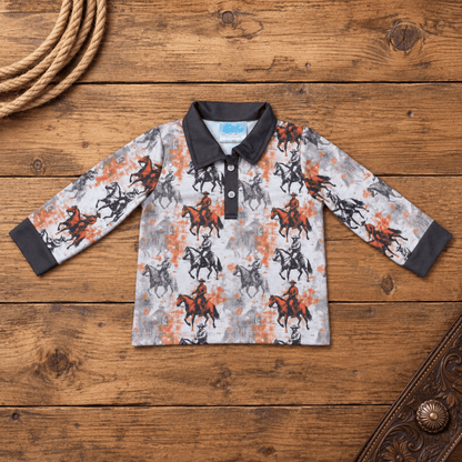 A long-sleeve polo shirt for kids, featuring a western-themed print of cowboy riders on horseback in black and orange on a light gray background. The shirt has a solid black collar and cuffs, and is displayed flat on a rustic wooden background with decorative rope and leather props.