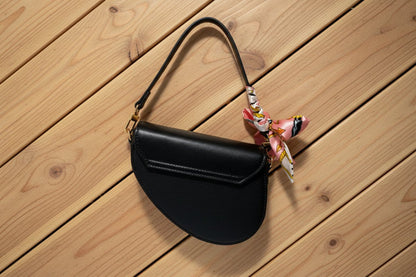 Black handbag with a colorful scarf attached to the handle on a wooden background
