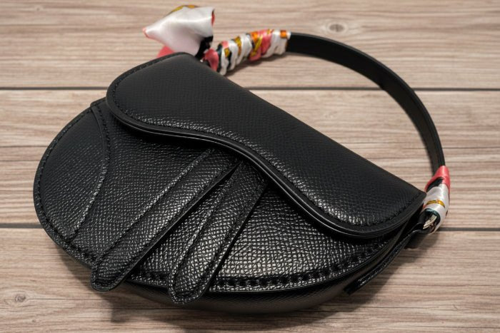 Black textured handbag with floral scarf on a wooden background