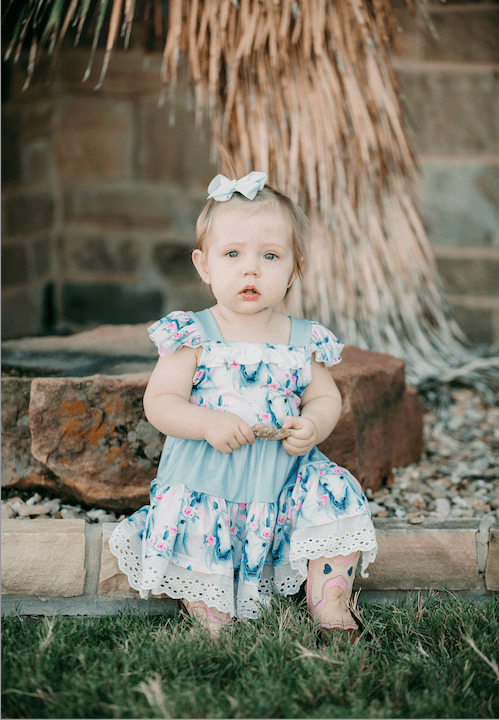 Young child in a floral & horse cowgirll dress sitting on stone steps outdoors.