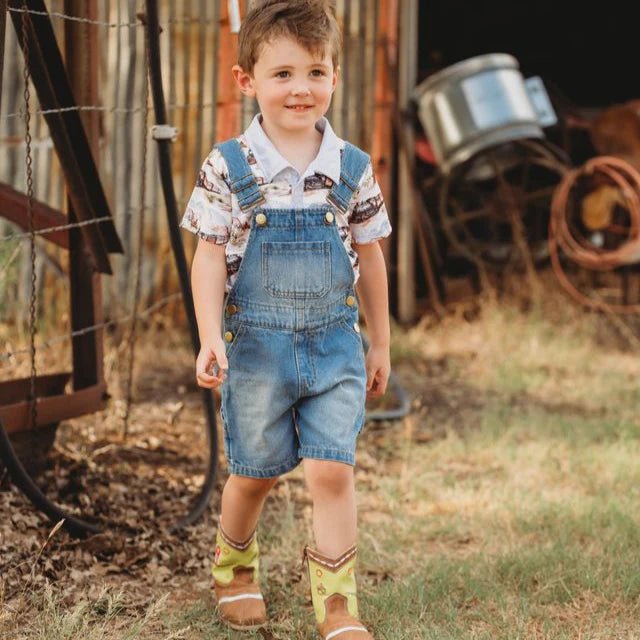 Child wearing denim overalls standing in a rustic outdoor setting with farm equipment.