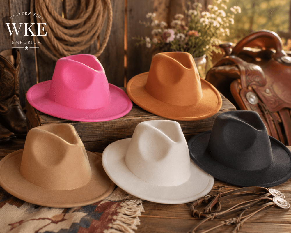 Five wide-brim fedora hats in pink, tan, cream, and black are arranged on a rustic wooden surface with western-themed props including a saddle, rope, and boots. The Western Rim Imports logo is visible in the top left corner.