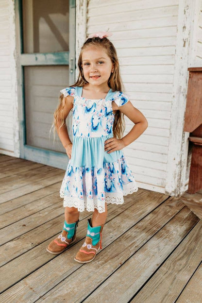 Young girl in a light blue horse head and flower dress  standing on a wooden deck.