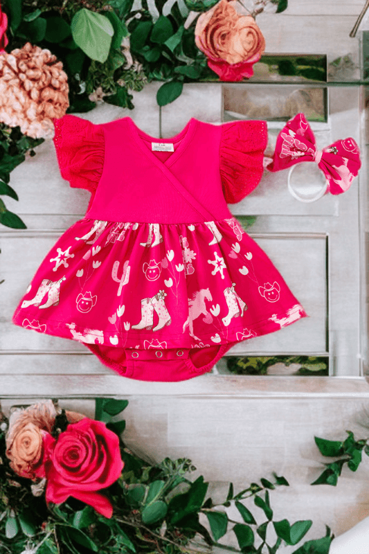 Fuschia baby dress with floral and animal pattern on a wooden surface with flowers around.
