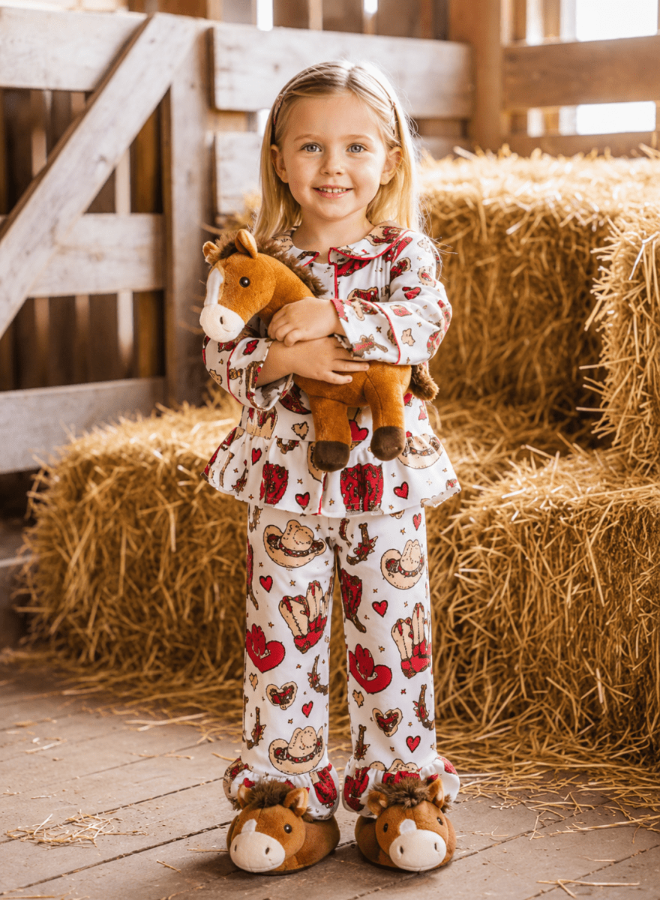 Young girl in pajamas holding a plush horse in a barn setting