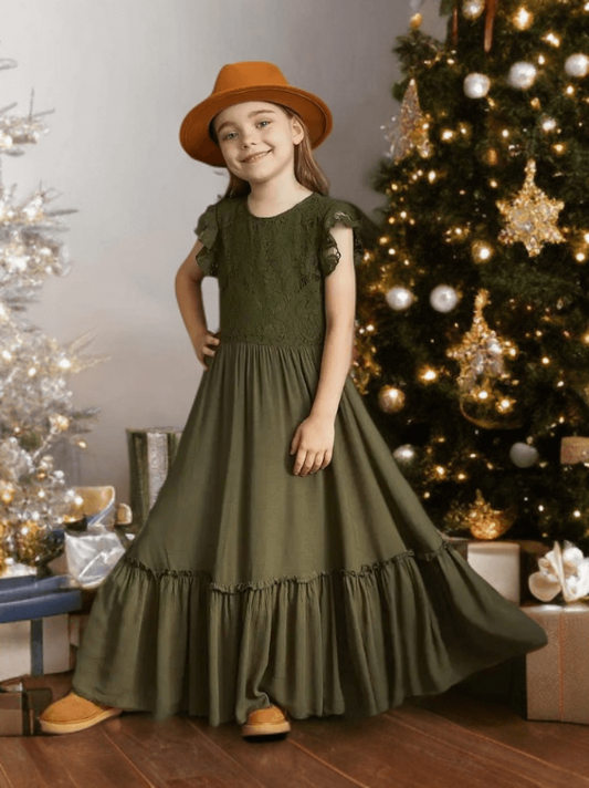 Young girl in a green dress and brown hat standing in front of a decorated Christmas tree.