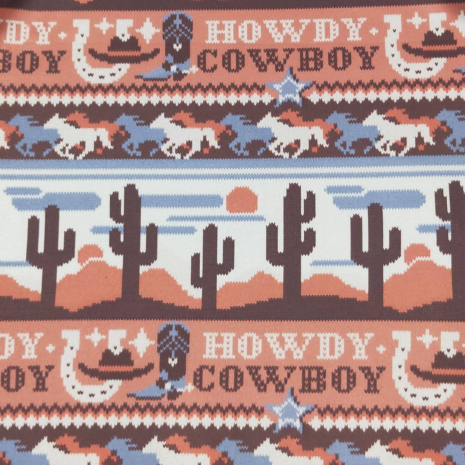 Patterned fabric with cowboy-themed design featuring horses, cacti, and text.