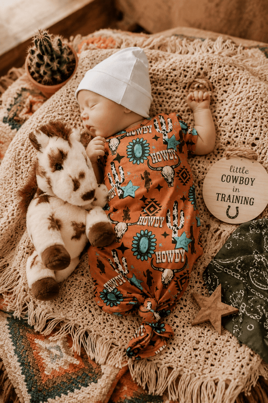 Baby in a cowboy-themed outfit with a horse and decorative elements on a textured blanket.