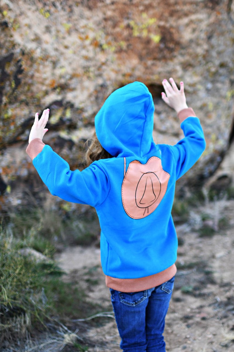 Person wearing a blue hoodie with a cowboy hat design outdoors