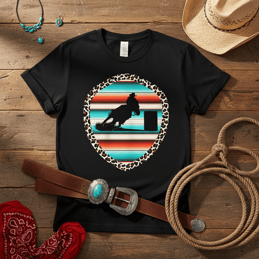 Black t-shirt with a graphic design of a person on horseback, surrounded by cowboy accessories on a wooden surface.