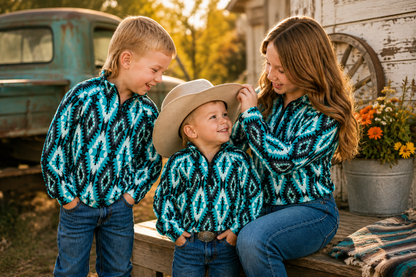 Three people wearing matching turquoise, black, and white geometric patterned long-sleeve button-up shirts, posed outdoors in a rustic setting with a vintage truck, wooden wall, and flowers.