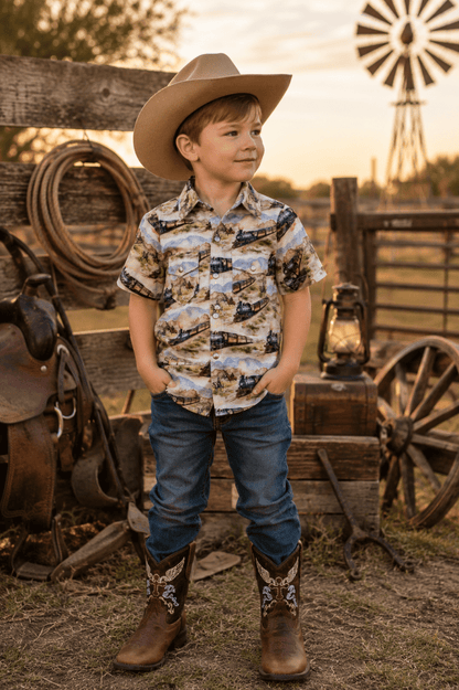 Young boy in cowboy clothing standing in a rustic outdoor setting with a windmill in the background.